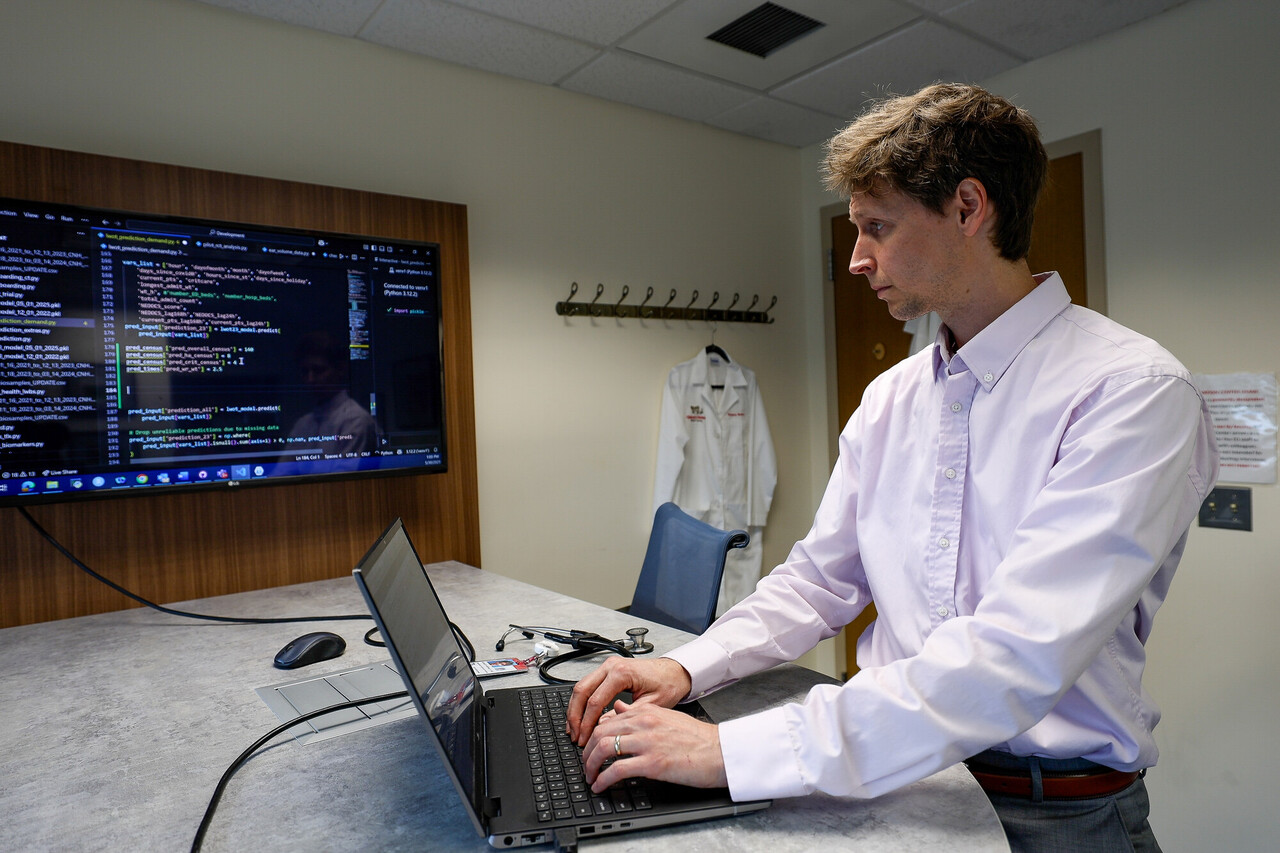 Man types on a laptop next to a code-filled wall display